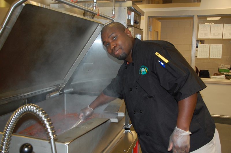 male cafeteria working stirring food in a large cooker