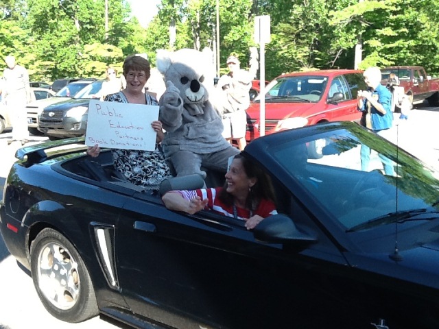 Adult female with mascot in back seat of convertible car