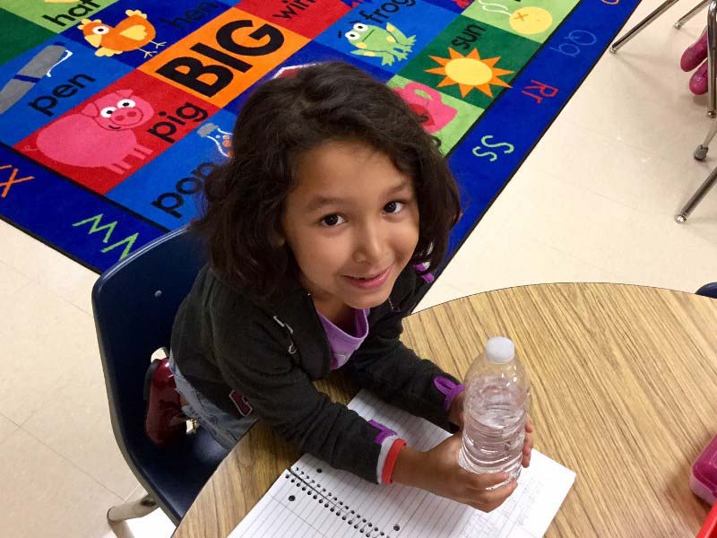 Female elementary student holding a bottle of water at a table