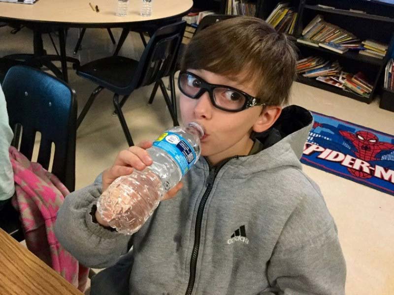 Male elementary student drinking water from a bottled water