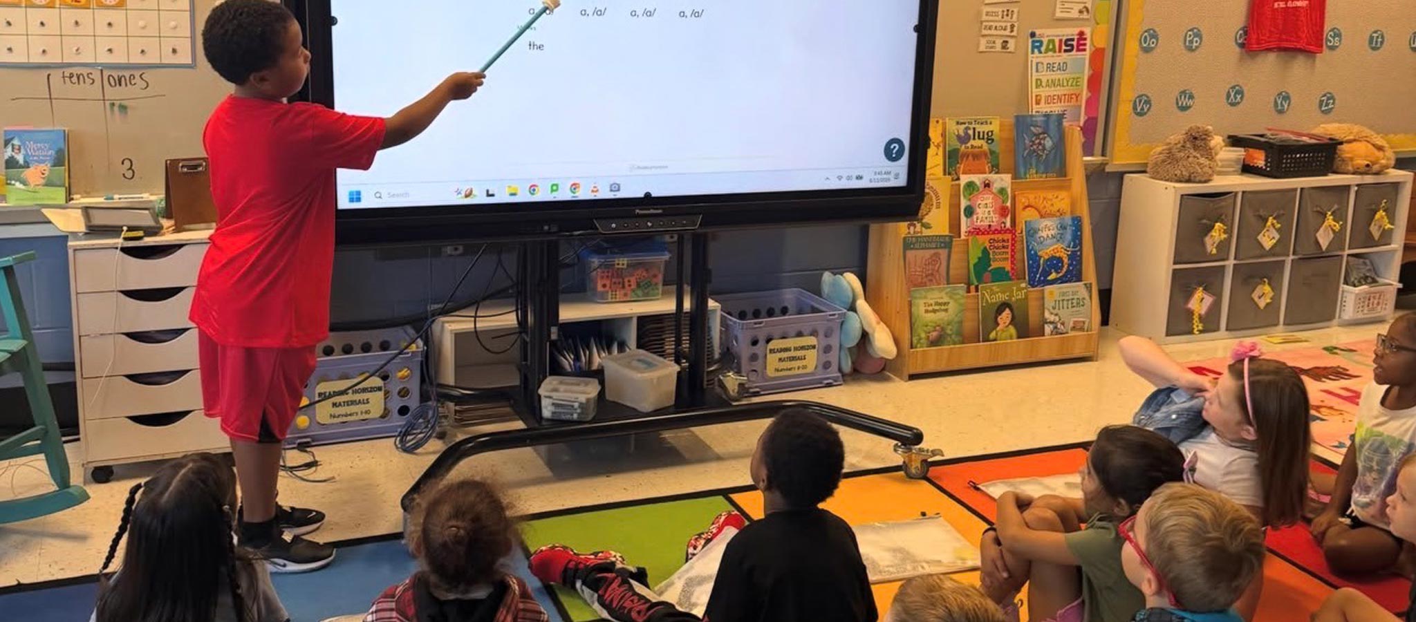 student using a pointer on a smartboard to teach fellow classmates