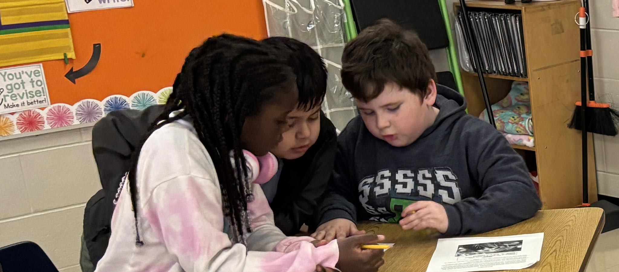 3 students working at a desk in the classroom