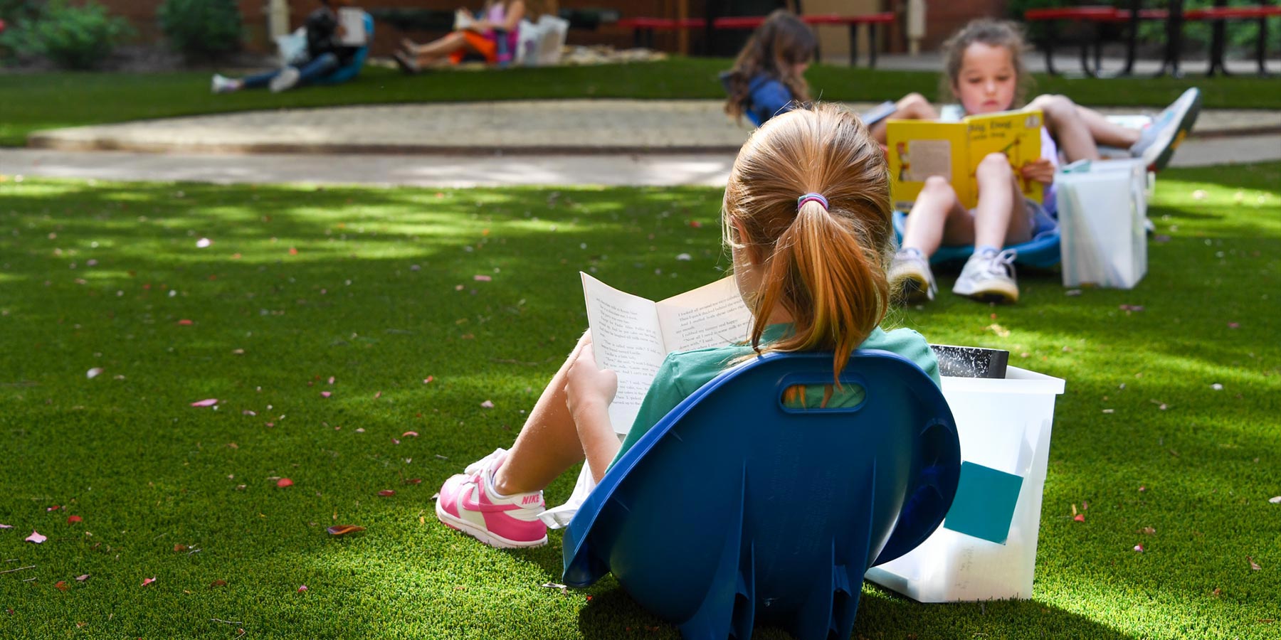 elementary girl sitting in grass reading a book