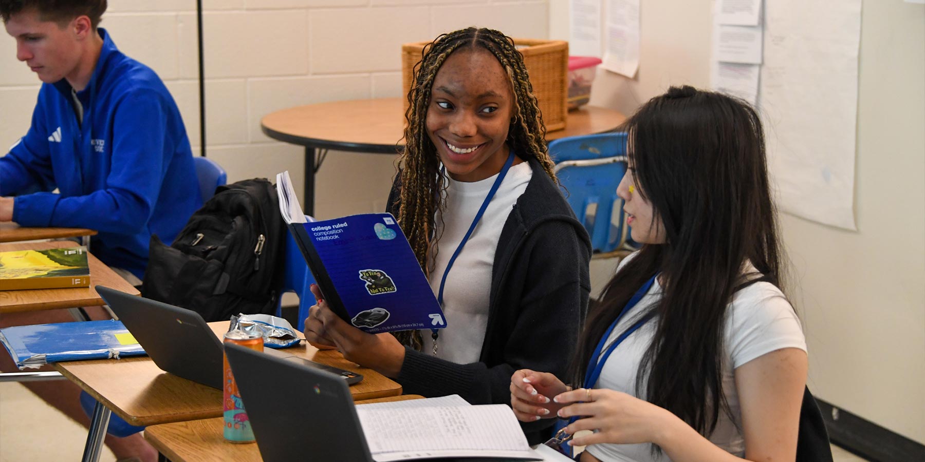 two high school girls at classroom desks conversing