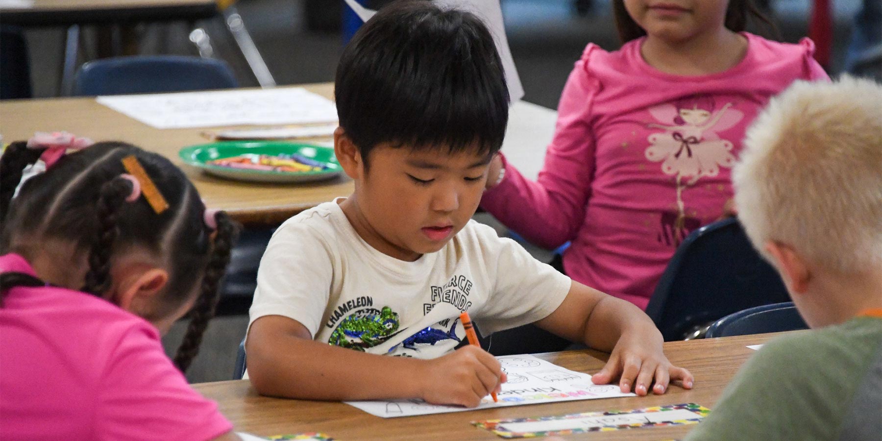 elementary boy drawing with a crayon on paper