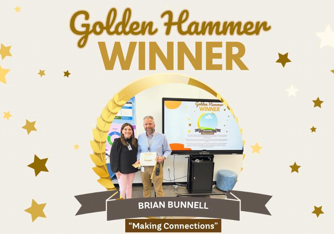 Golden Hammer Award Winner Brian Bunnell with another adult holding a certificate in front of a promethean board. 