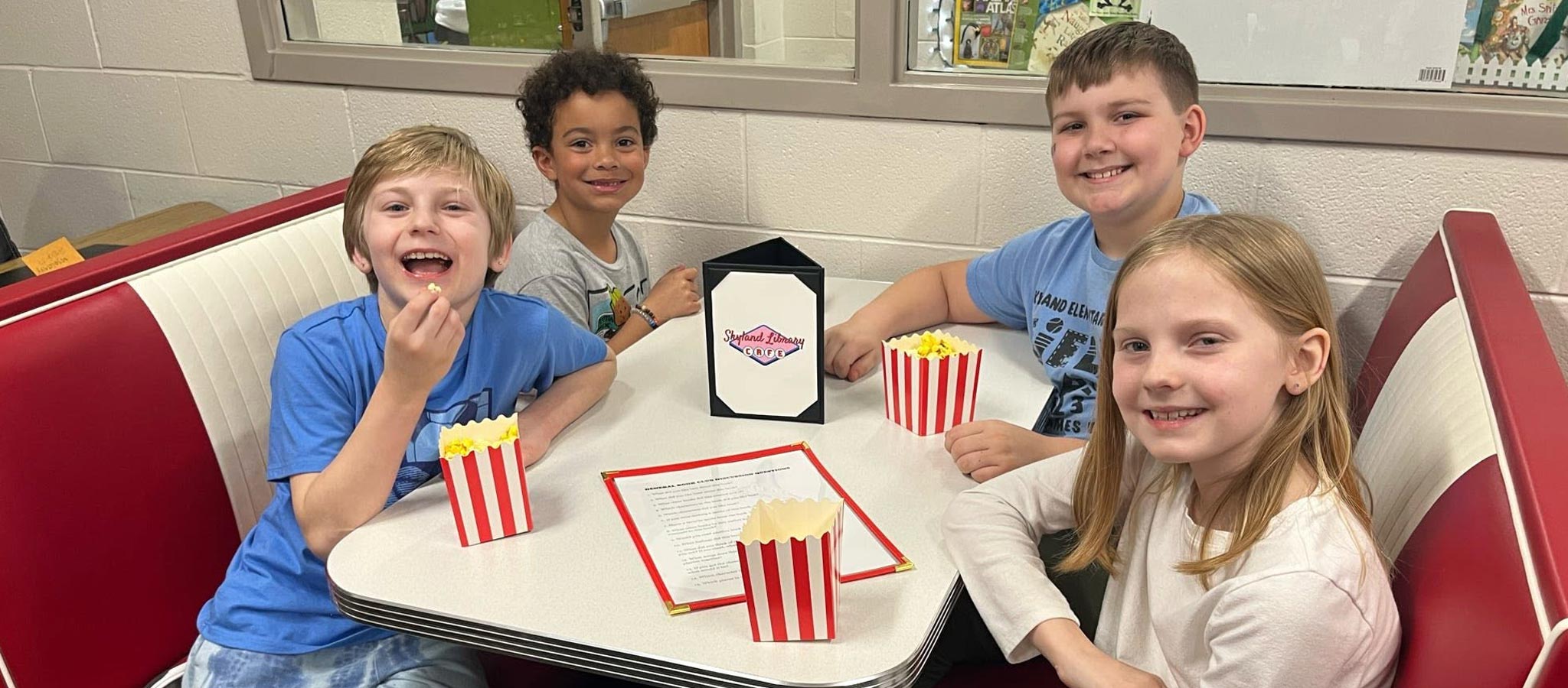4 students sitting at a table eating popcorn