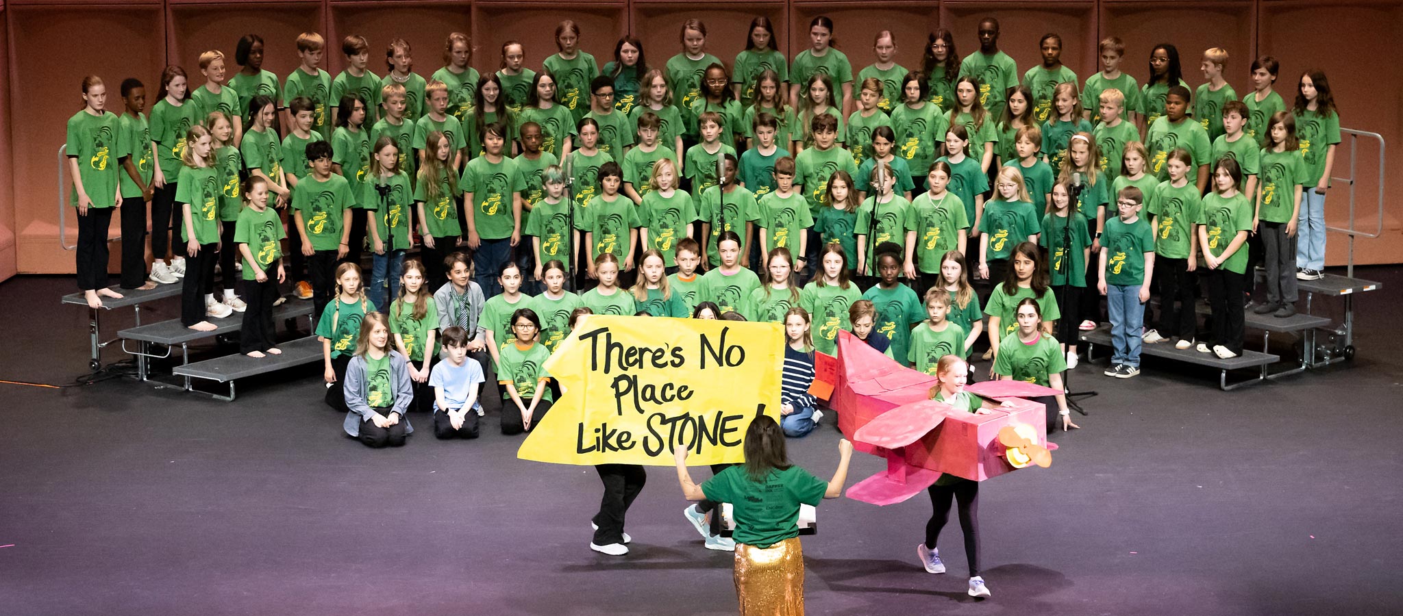 large group of elementary choir students wearing green shrits with teacher leading