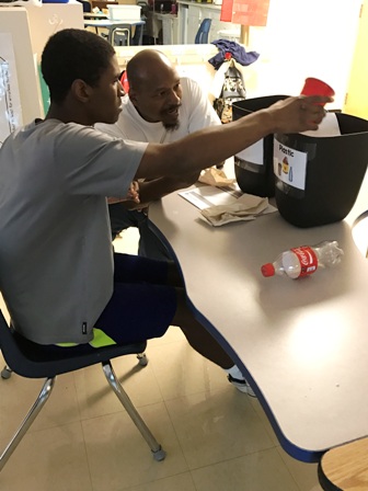 Washington Center student Jace Randall, assisted by Para-Educator Lopez Bryant, practices life skills by sorting items for recycling. 